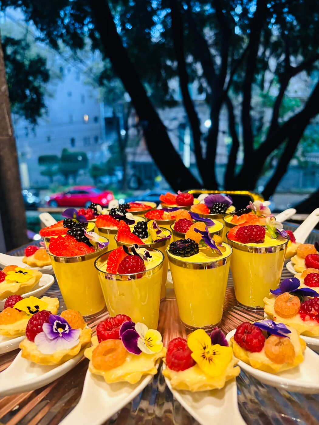Vasitos de postre de mango con frutos rojos y flores comestibles en evento social